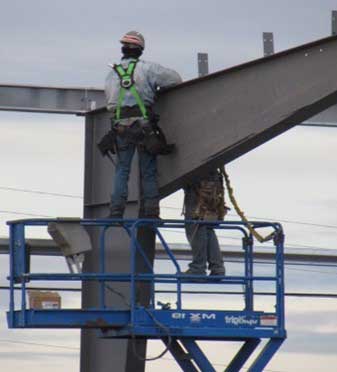 Shows a worker standing on the guardrail of an Aerial Work Platform